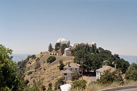 [This image was taken slightly above the level of the observatory. The observatory and its buildings are atop a flattend mound with steep drop offs around it. The houses are two story white building off to one side.]